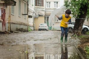 boy in laneway with umbrella and gumboots splashing in puddle